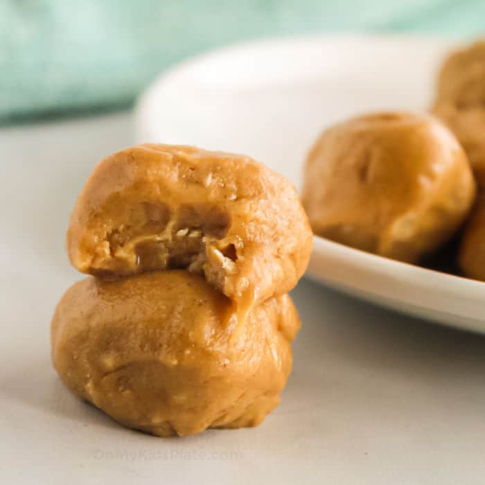 Peanut butter snack bites stacked by a plate, one with a bite missing.