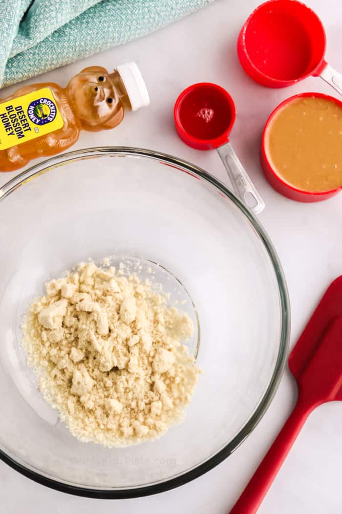 Adding almond flour in a bowl with other ingredients next to the bowl