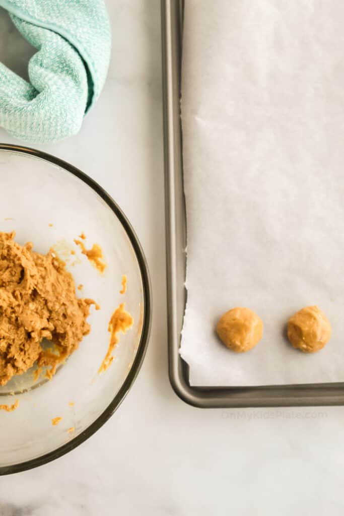 Rolling peanut butter dough into balls on a cookie sheet