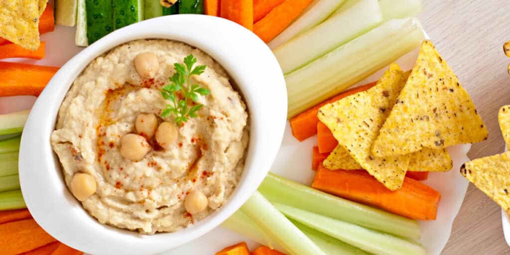 A tray of hummus with vegetables and chips