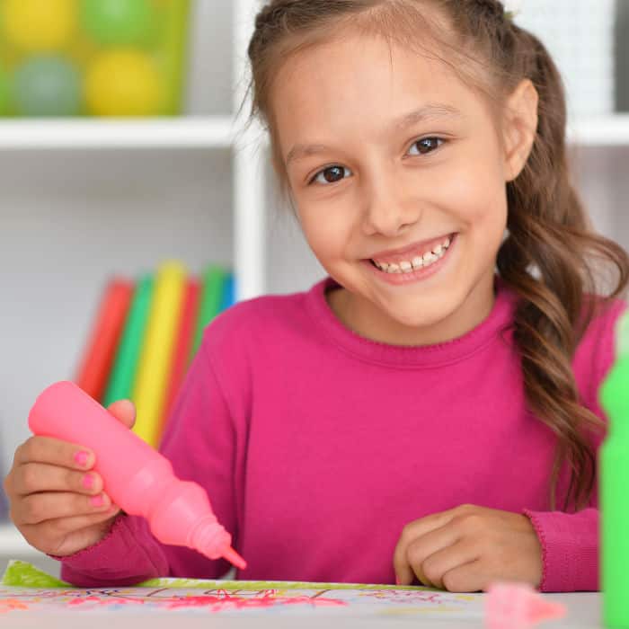 A little girl smiling at the camera painting with paint pens