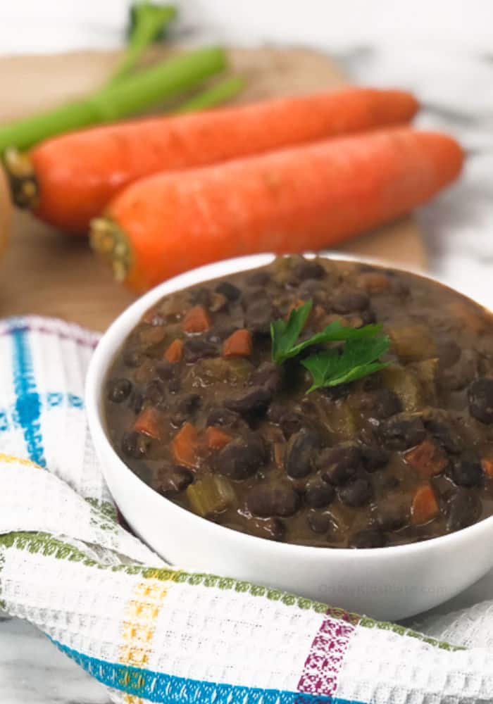 A bowl of black bean soup with carrots and celery in the background