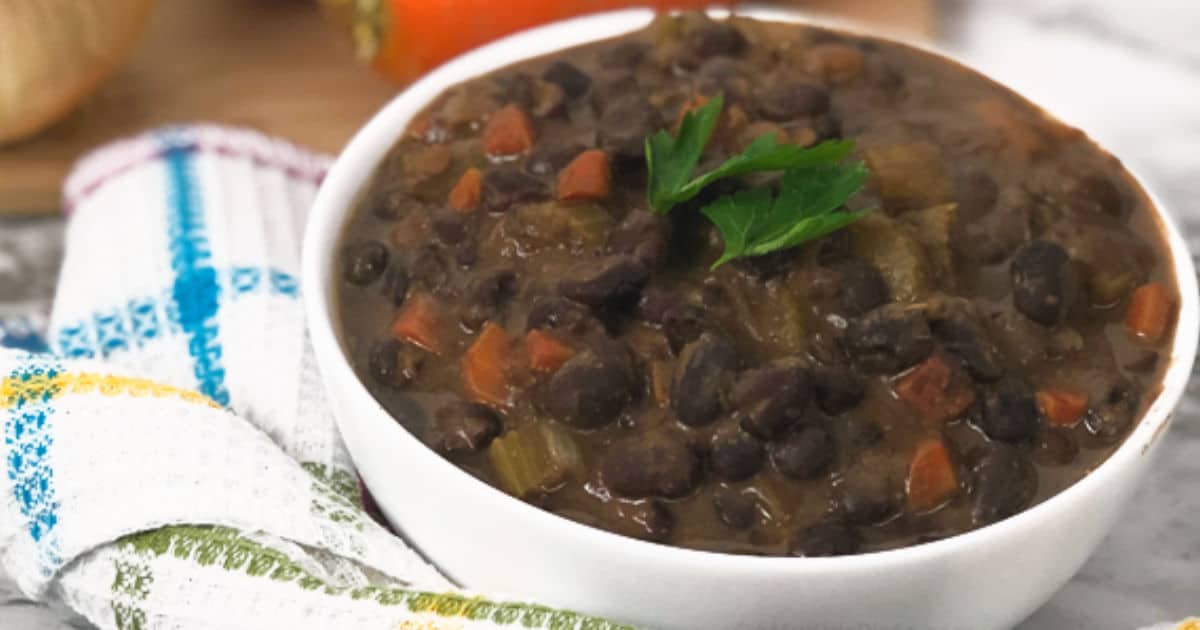 A close up side view of a bowl of black bean soup with parsely on top, with a kitchen linen on the side.