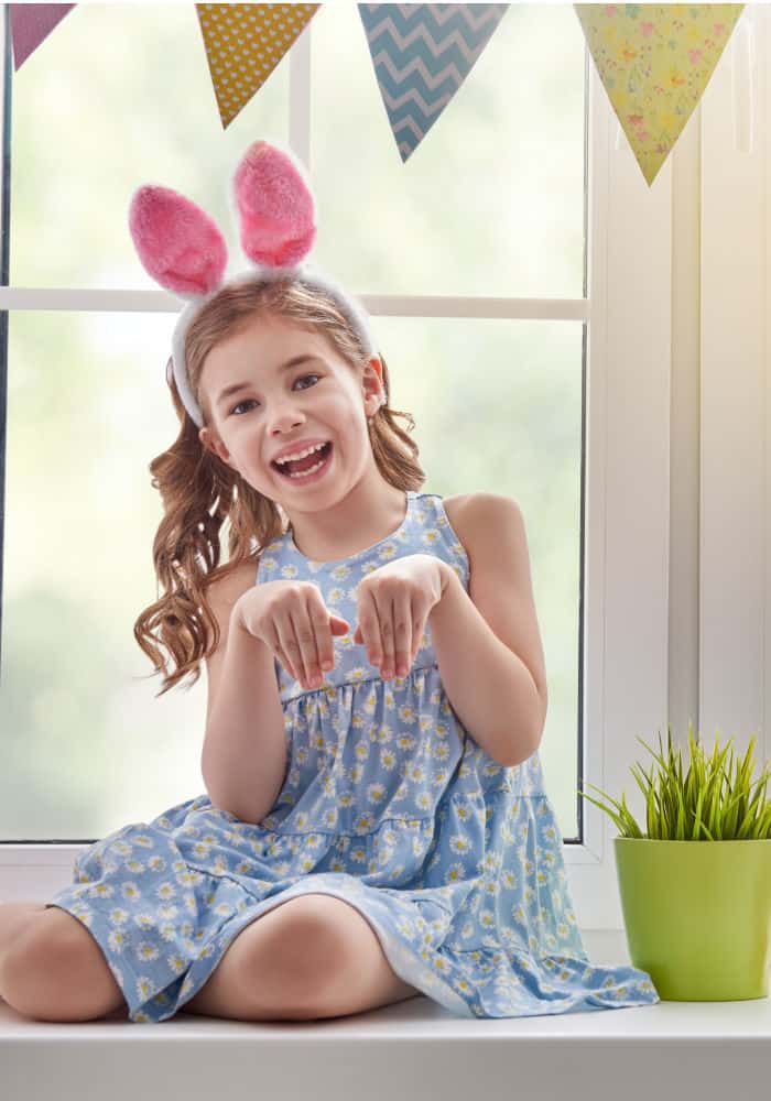 A little girl sitting in front of a window pretending to be a rabbit
