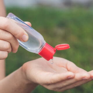 A person's hands holding a small bottle of DIY hand sanitizer and squeezing it into their hand