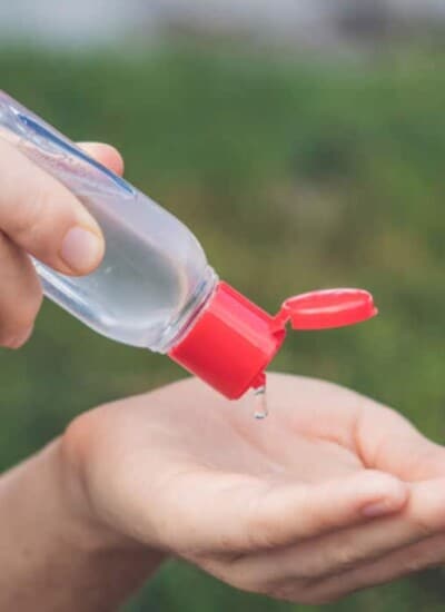 A person's hands holding a small bottle of DIY hand sanitizer and squeezing it into their hand
