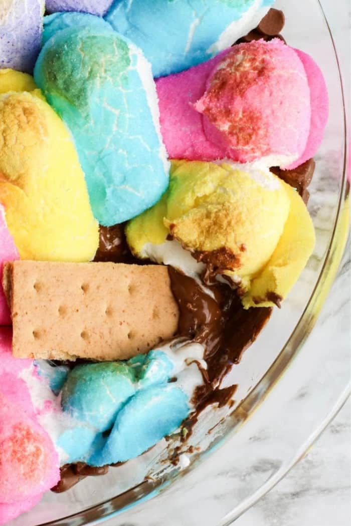 A graham cracker dipping in melted chocolate and peeps marshmallows