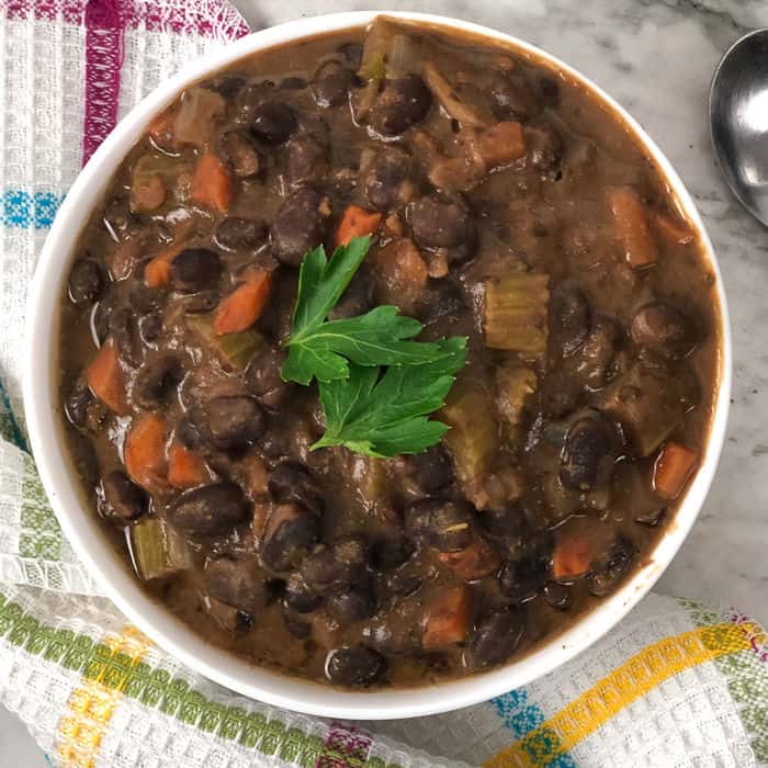 A close up overhead shot of black bean salsa soup. A kitchen towel is on the side of the bowl and a spoon is off to the side.