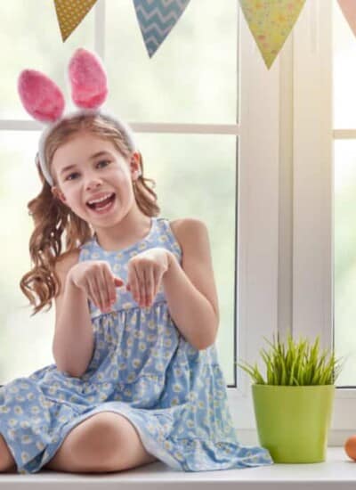 A little girl in front of a window wearing bunny ears pretending to be a rabbit