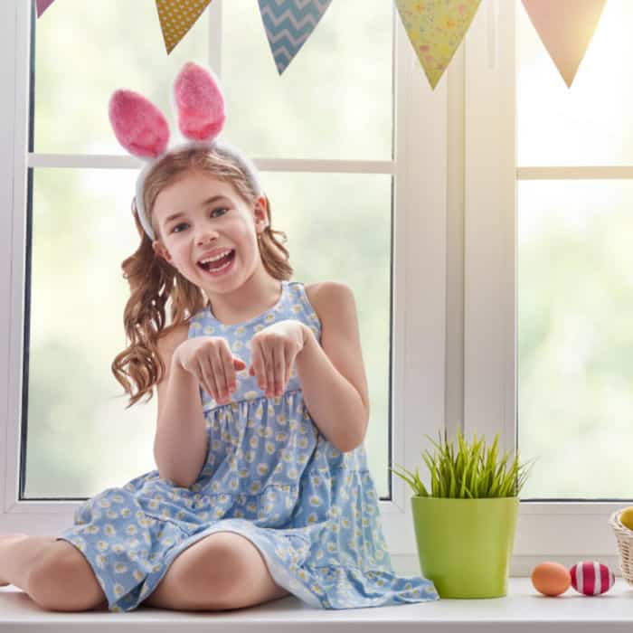 A little girl in front of a window wearing bunny ears pretending to be a rabbit