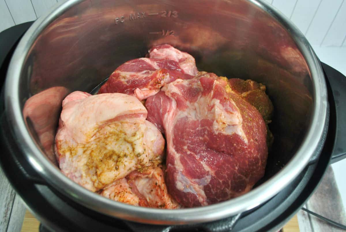Raw pieces of pork with seasonings are placed inside a stainless steel Instant Pot, ready to create flavorful Instant Pot Pork Carnitas on a wooden surface.