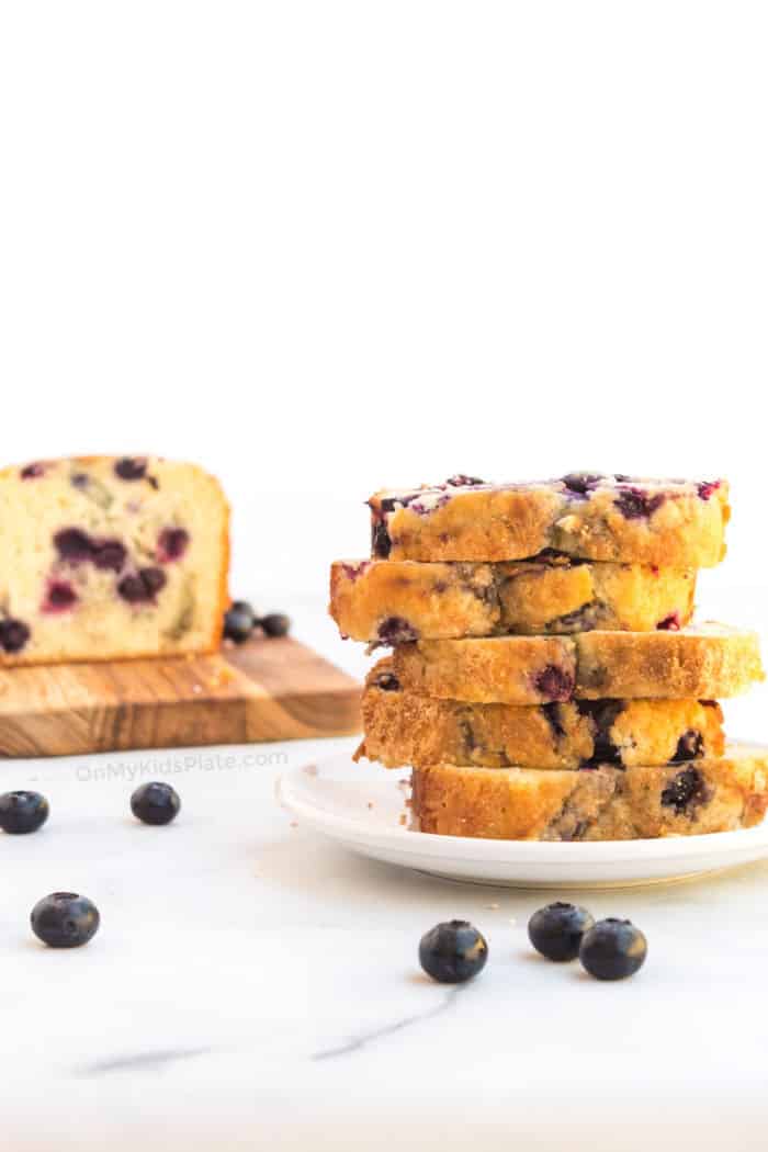 Blueberry bread sliced stacked high on a plate with more slices on a cutting board