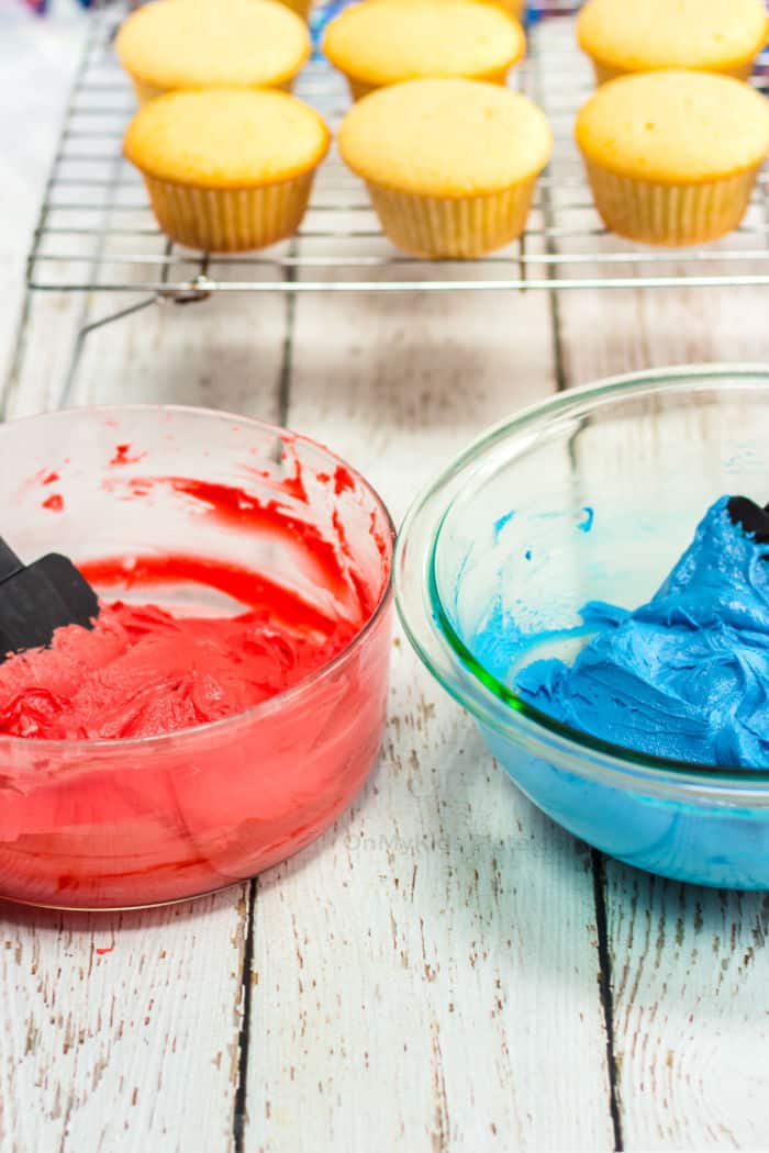 Red and blue frosting being mixed with cupcakes behind