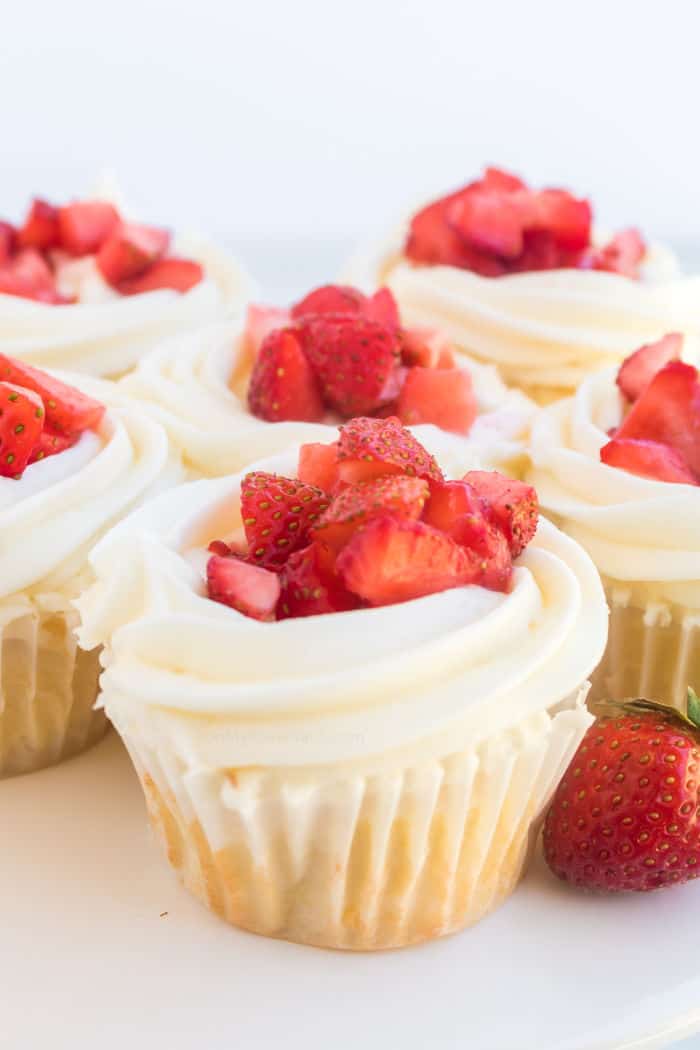 Several cupcakes frosted topped with fresh strawberry pieces.