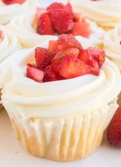 A cupcake with frosting and fresh strawberry pieces on top