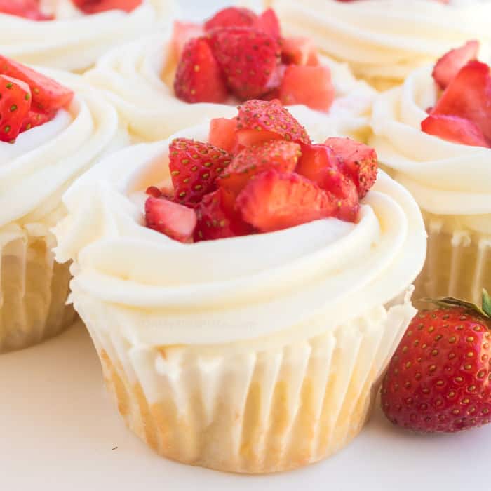 A cupcake with frosting and fresh strawberry pieces on top