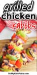 Grilled chicken kabob skewers are on a wood serving platter juicey and delicious next to a red kitchen linen. A text title overlay reads grilled chicken kabobs.