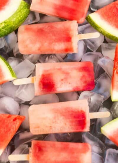 A close up view of watermelon Popsciles and slices of watermelon on a tray full of ice.