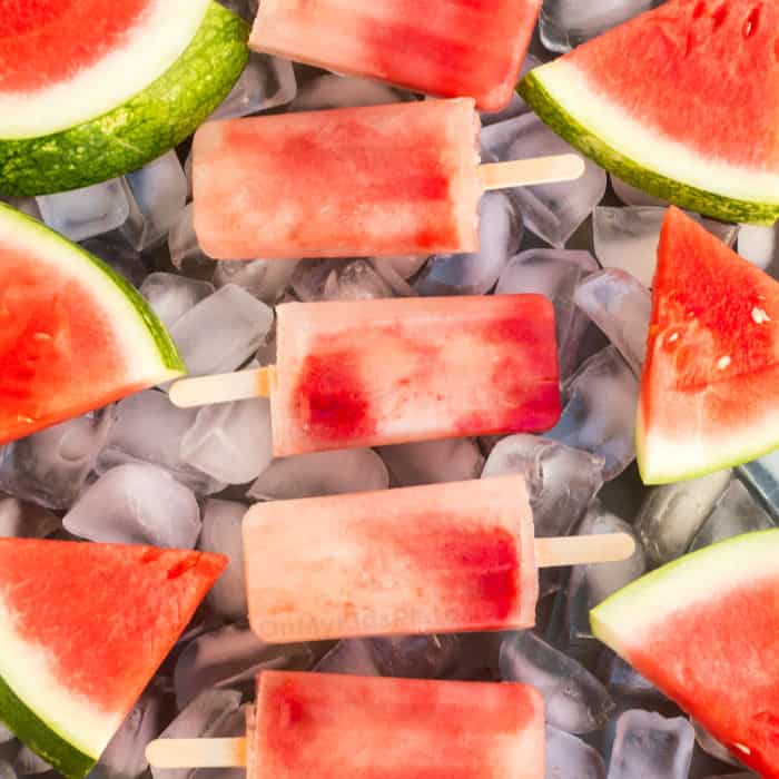 A close up view of watermelon Popsciles and slices of watermelon on a tray full of ice.