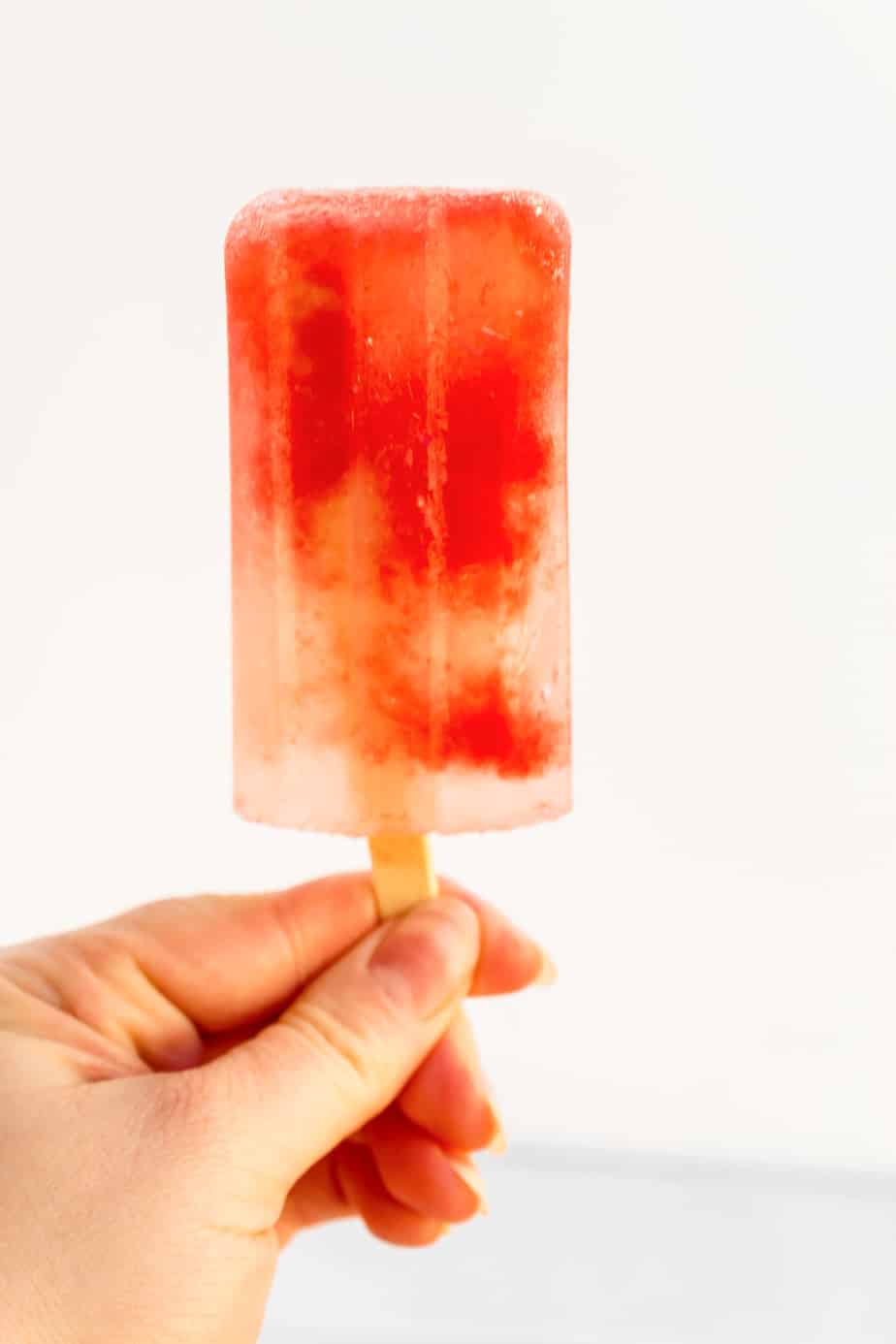 A watermelon popsicle being held by a hand from the side against a white background.