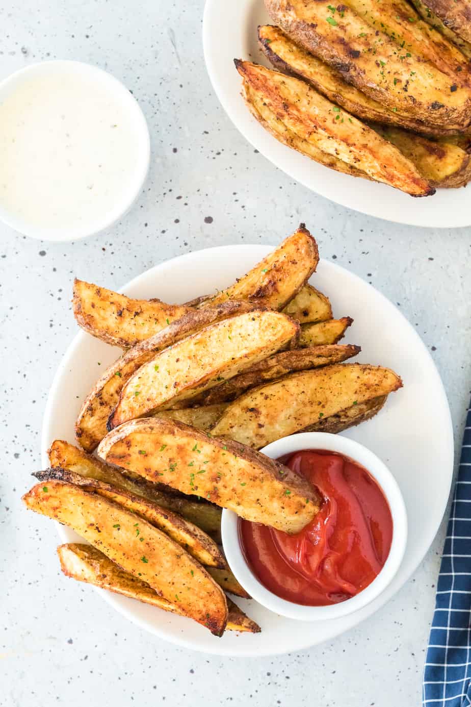 Crispy potato wedges on a serving platter from overhead with bowls of ketchup and ranch for dipping on the table