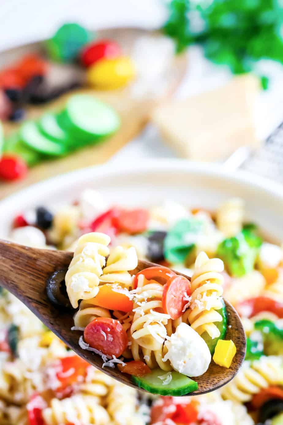 Italian pasta salad being scooped from the bowl with a wooden spoon close up.