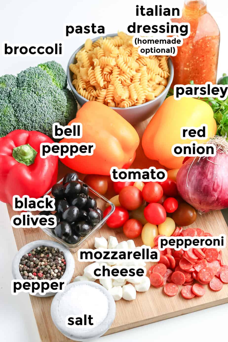 Ingredients for italian pasta salad on a cutting board in bowls from the side with labels.