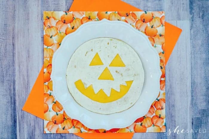 A tortilla with a jack-o'-lantern face made into a quesadilla on a plate.