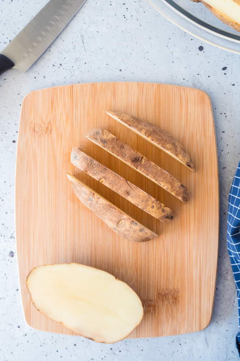 Slicing a potato on a cutting board in half and the half into four equal wedges.