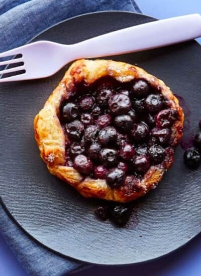A blueberry galette on it's own plate with a fork and napkin