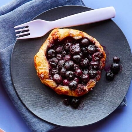A blueberry galette on it's own plate with a fork and napkin