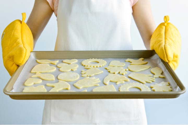 women holds a tray of raw cookies on a pan with yellow oven mitts
