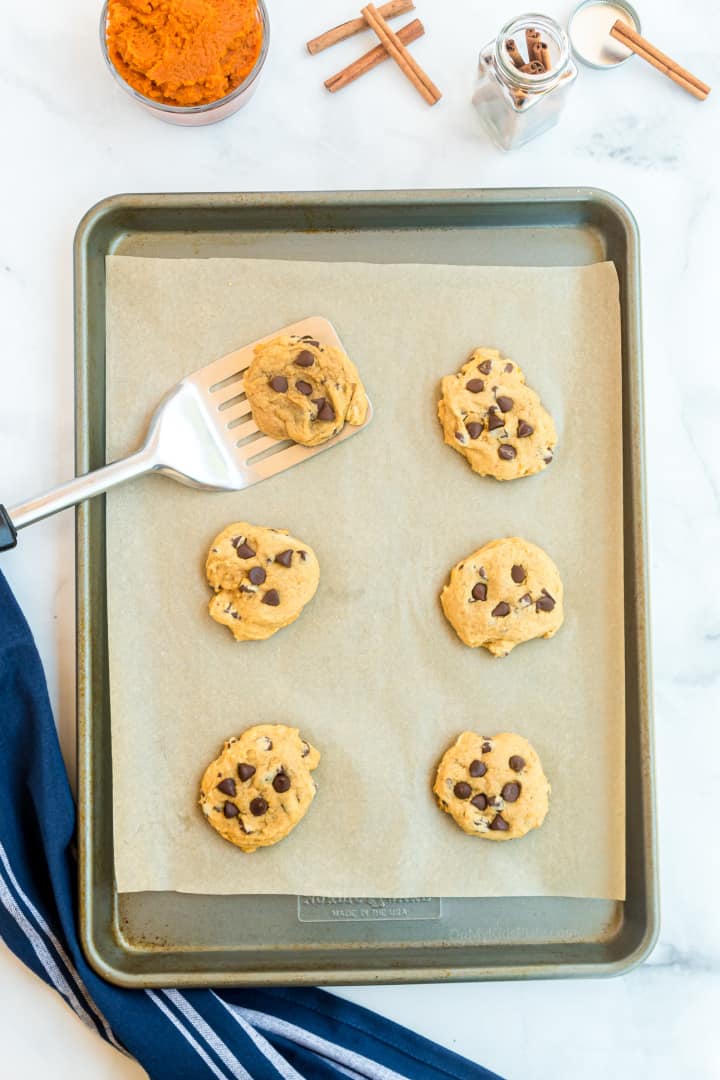Cookies on a pan freshly baked with a spatula picking one cookie up. Pumpkin and cinnamon sticks are on the counter.