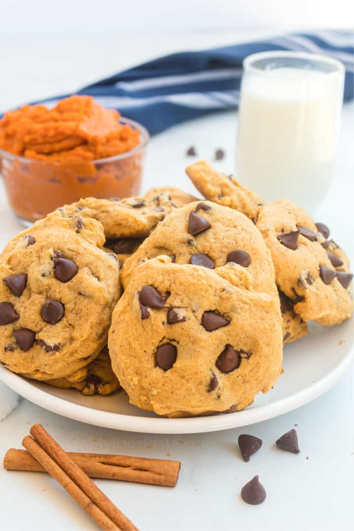 A plate full of pumpkin chocolate chip cookies with mashed pumpkin and milk in the background.