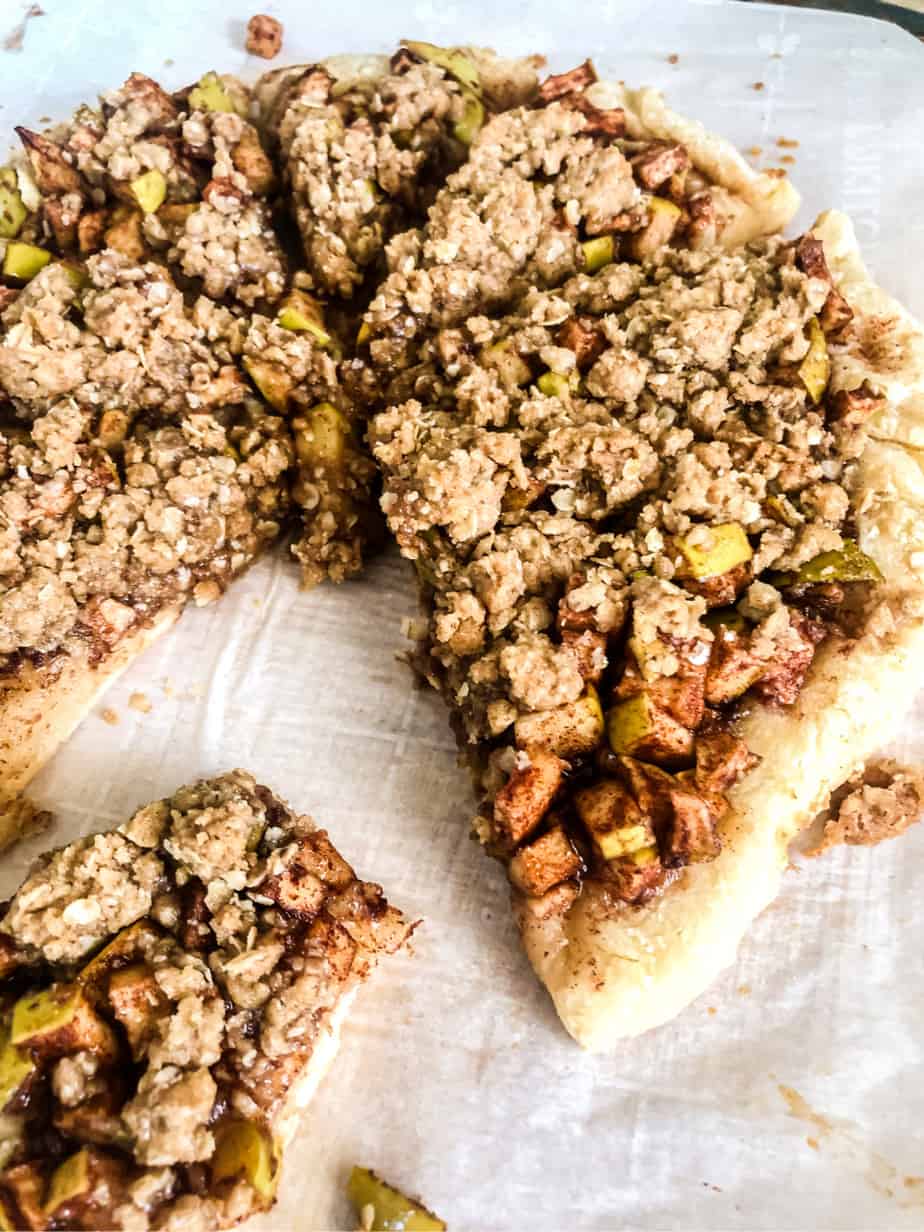 Close up of apple dessert pizza sliced on parchment paper with a crumble topping.