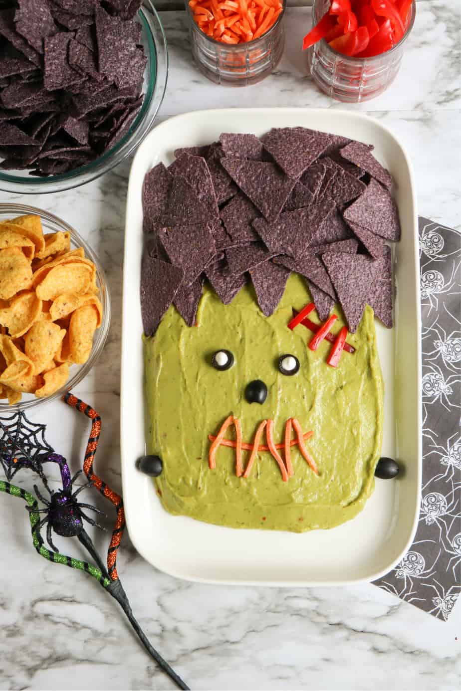 Plater of guacamole decorated to look like Frankenstein with jars of chips and veggies to dip in bowls