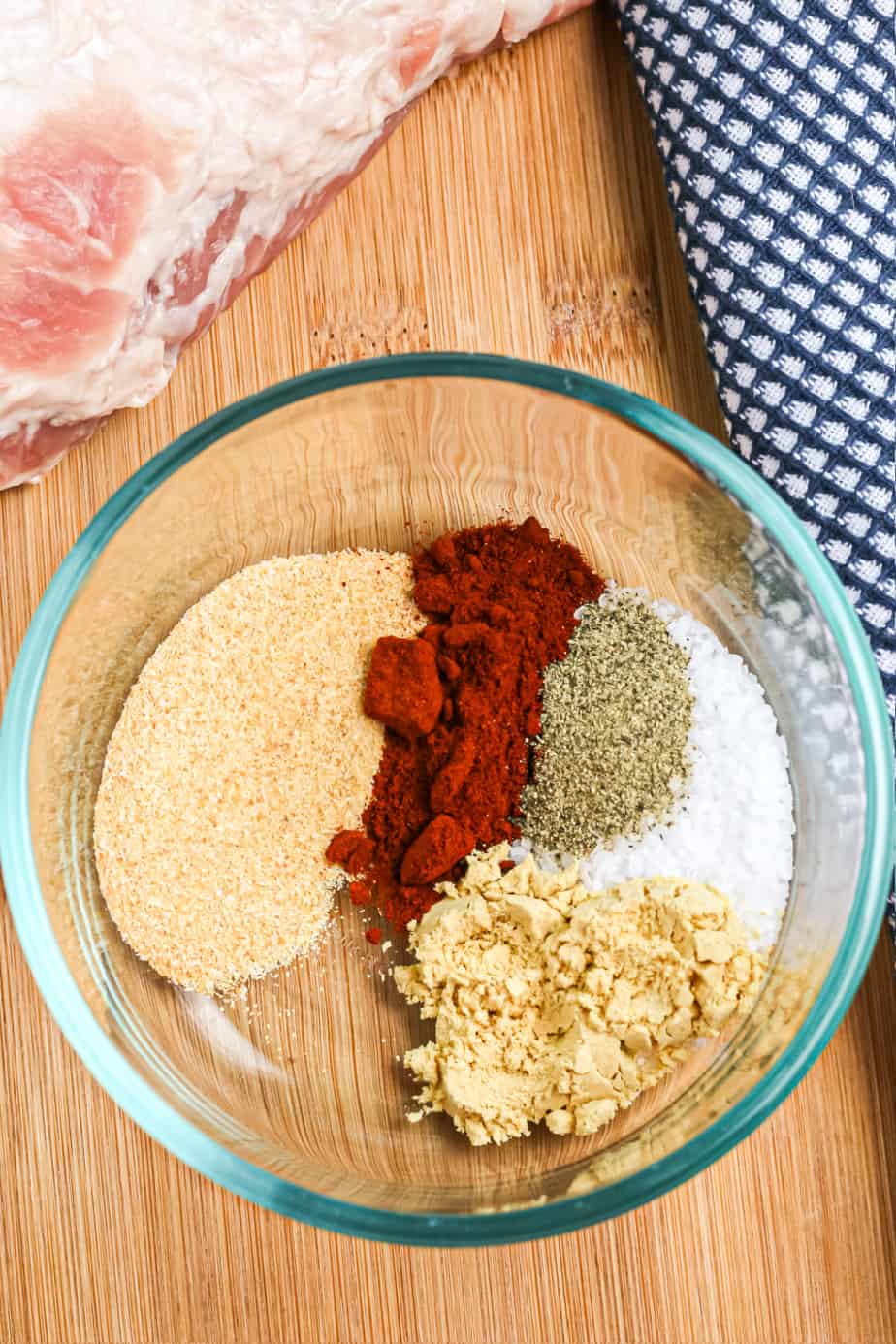 Spice rub in a bowl before mixed below a pork loin on a cutting board.