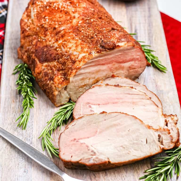 Close up of sliced pork loin on a serving platter with rosemary.