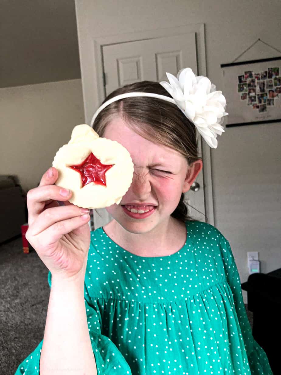 Girl holds stained glass sugar cookie up to her eye looking through it.