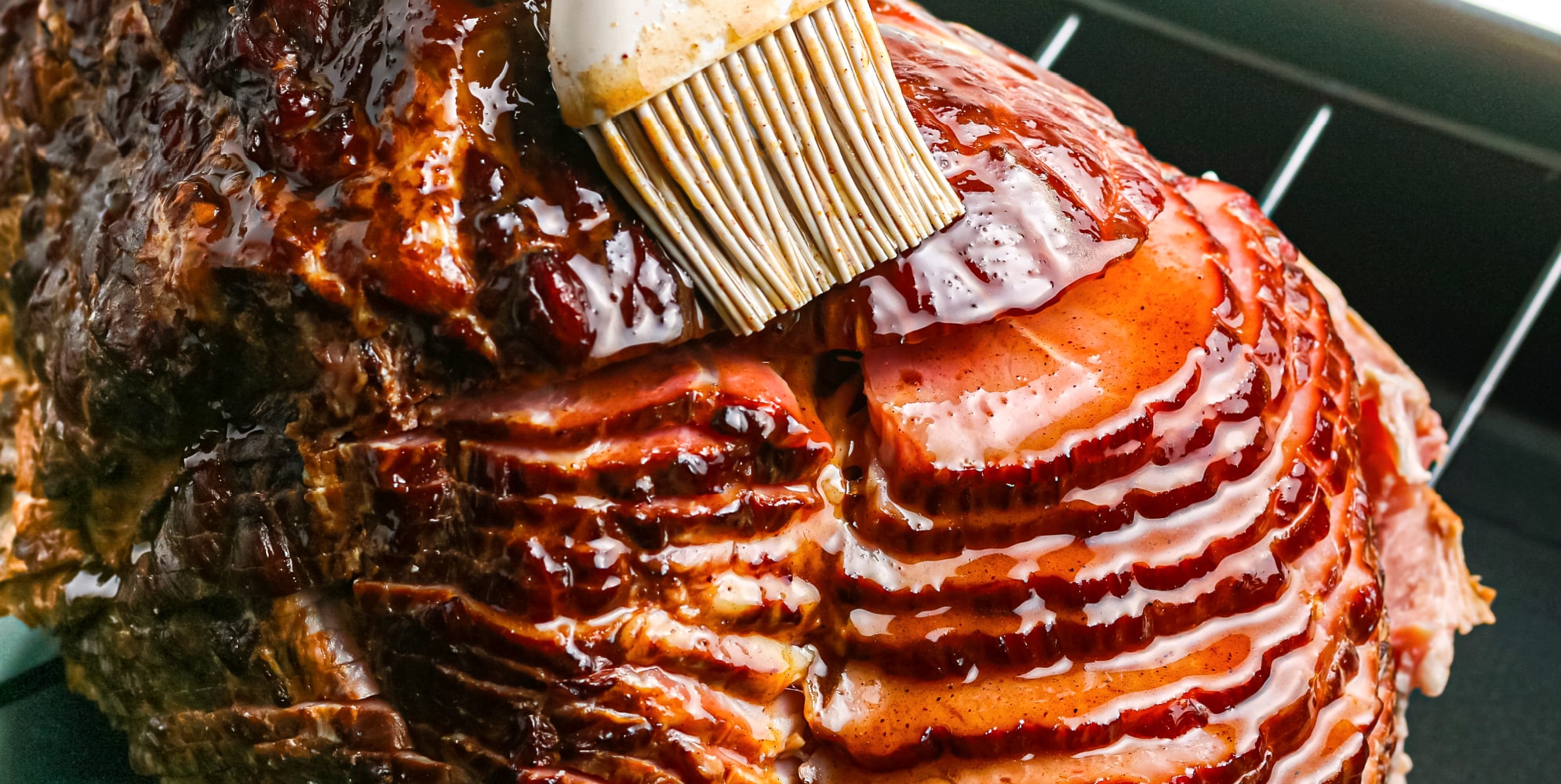 A ham being cooked in a pan with a brush, perfect for the ham sauce recipe.