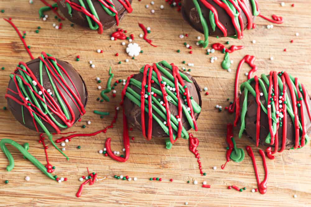 Hot cocoa bombs being decorated with Christmas colored chocolate drizzles and lots of sprinkles.