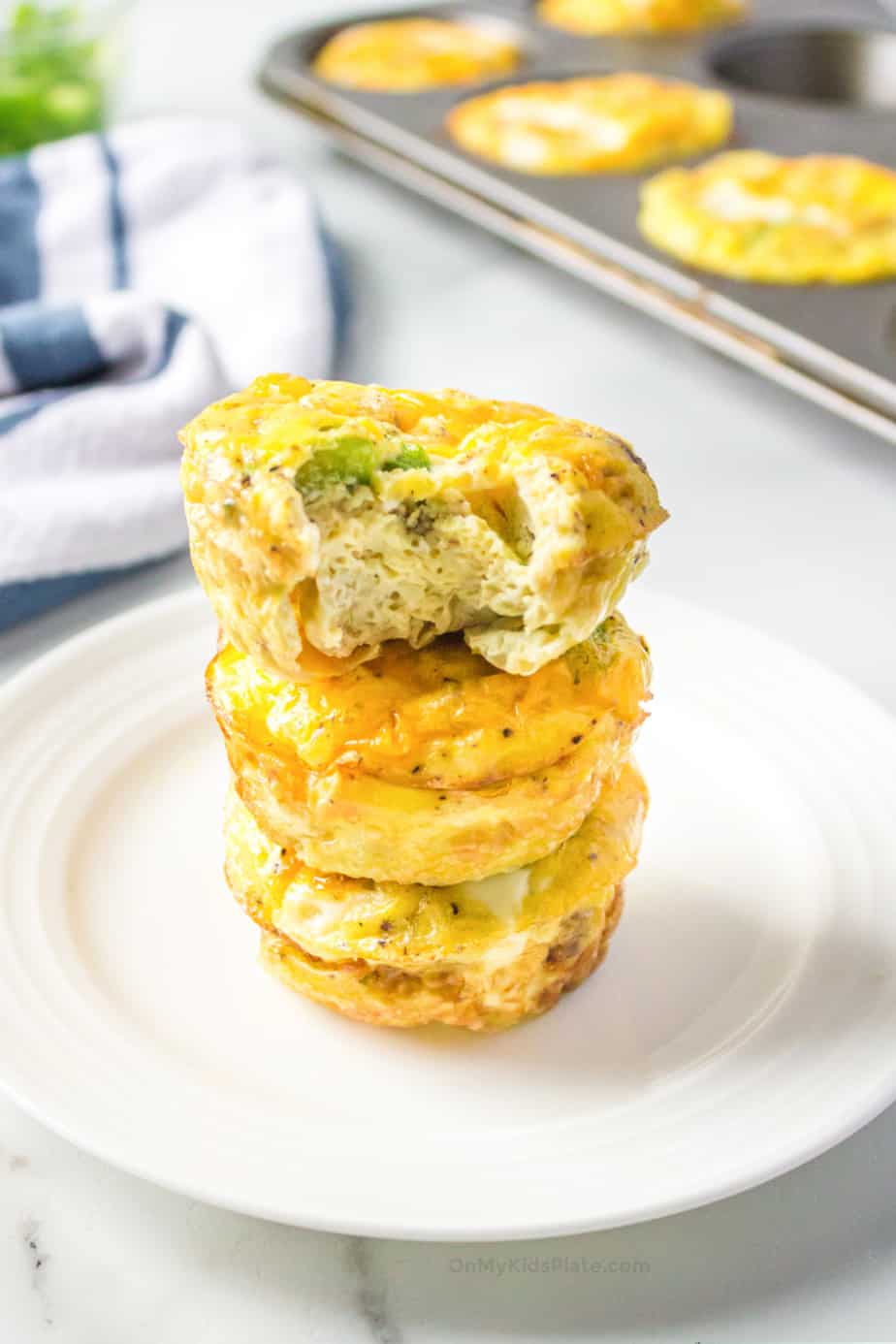 Stacked egg muffins on a plate with a bite taken out to see the sausage and bell pepper
