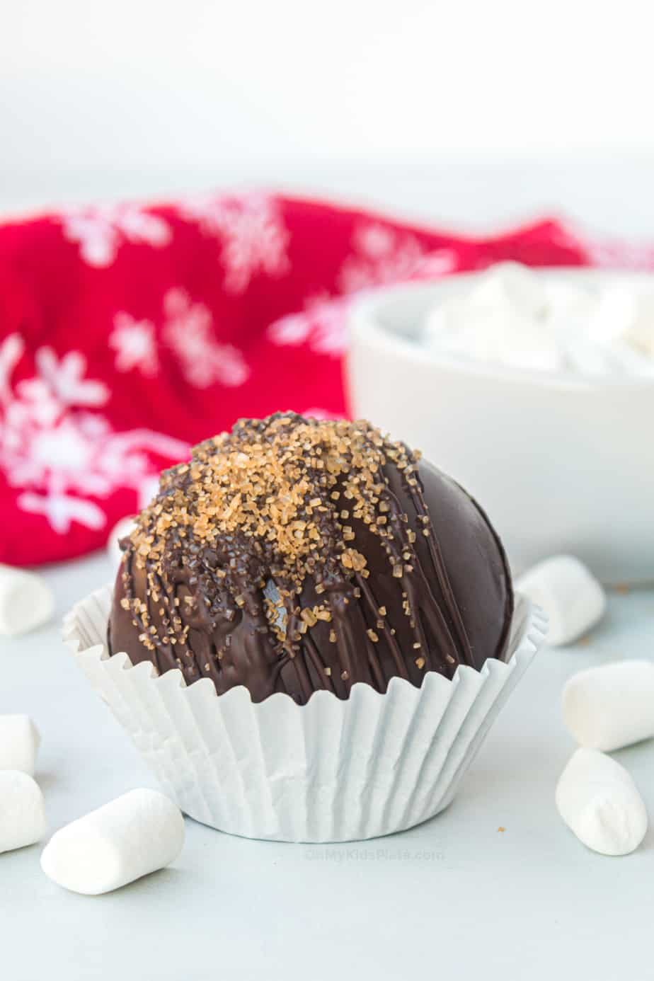 Hot chocolate bombs in a cupcake liner decorated with drizzled chocolate and raw sugar.