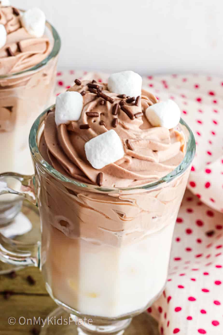 A glass of whipped hot chocolate topped with marshmallows and sprinkles