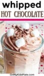 A large glass of creamy chocolate drink with marshmallows and sprinkles and title text on ge.top of the ima