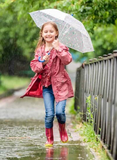 Little girl jumps laughing in spring puddles with an umbrella