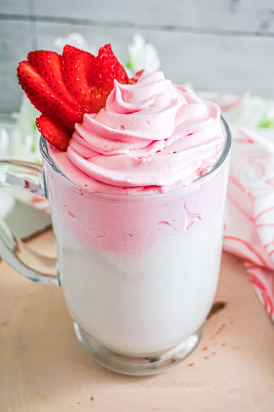 Close up of a tall glass of pink whipped strawberry milk topping over milk topped with fresh strawberries