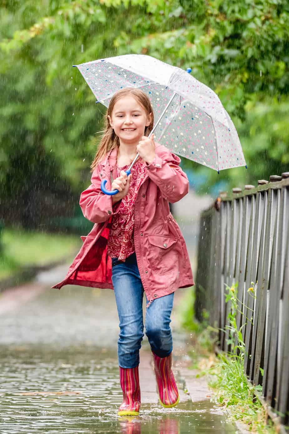 Girl with umbrella laughs jumping in spring puddles
