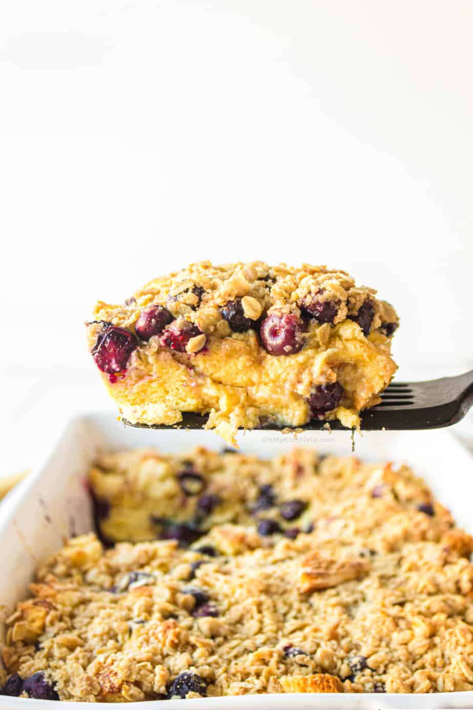 A slice of baked blueberry french toast casserole being lifted from the pan from the side so you can see the layers.