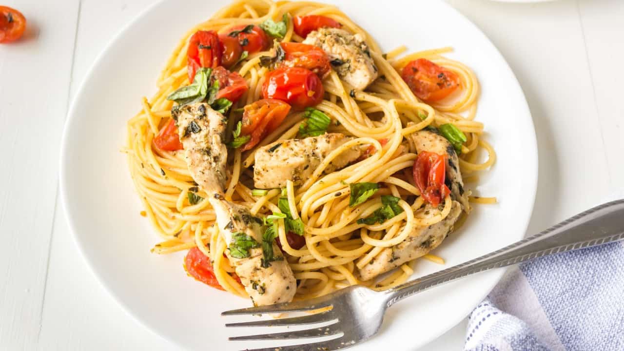 Fork and plate of pasta with chicken, tomatoes and spinach.